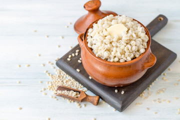 Barley porridge with butter in a small earthen pot on a light wooden table. Selective focus.