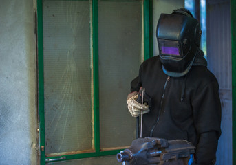 Obraz premium Worker with protective gloves and protective mask welding metal part in workshop