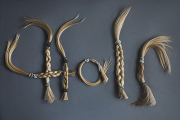 HAIR written with chopped off blond braided hair on a gray background