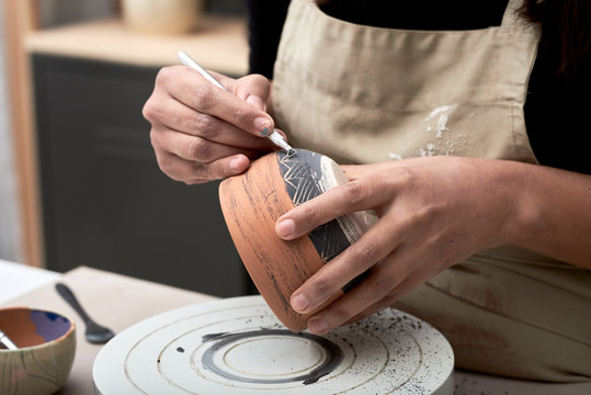 Artisan decorating clay pot with tool