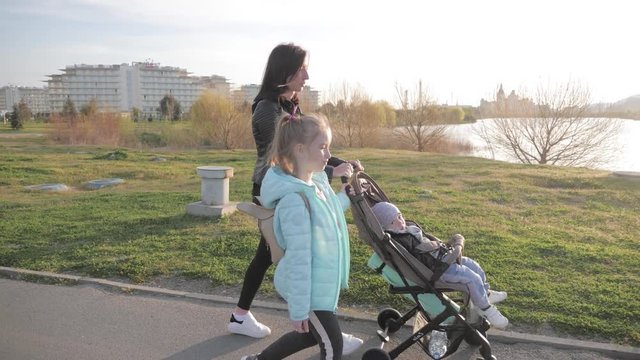 Mother with baby stroller and two kids taking a walk down the street.