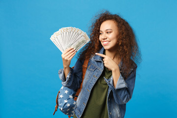 Young african american girl teen student in denim clothes, backpack hold cash money isolated on blue background studio portrait. Education in high school university college concept. Mock up copy space