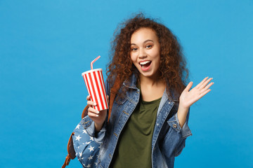 Young african american girl teen student in denim clothes, backpack hold paper cup isolated on blue background studio portrait. Education in high school university college concept. Mock up copy space.