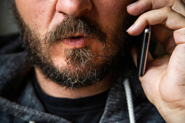 Close up portrait of bearded man talking on smart phone, focus on lips, no eyes, secret talk,...
