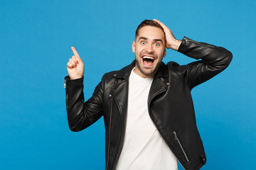 Handsome stylish young unshaven man in black jacket white t-shirt showing on workspace isolated on blue wall background studio portrait. People sincere emotions lifestyle concept. Mock up copy space.