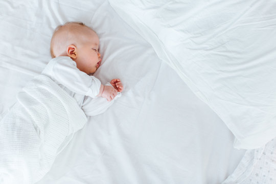 A baby boy asleep on his side on a big bed after a daytime feed