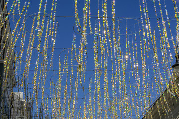  festive glitter ribbons with gold circles against building facade and blue sky. Colorful garland for city event decoration