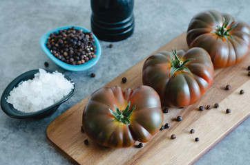 Whole Sweet Marmande tomatoes on wooden board and stone background.