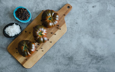 Whole Sweet Marmande tomatoes on wooden board and stone background. Copy space.