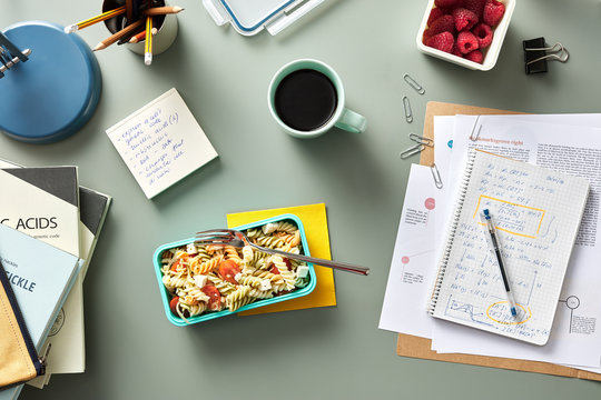 Delicious homemade pasta in container with cup of coffee on desk