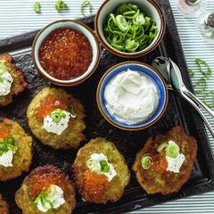 Russian traditional potato pancakes served with red caviar, green onions and sour cream on a tray with white wine and lemon