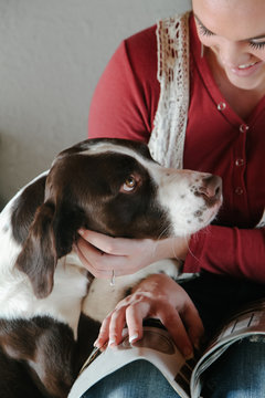 smiling woman pets dog while reading magazine