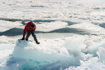 Boy carefully climbs across chunks of ice on frozen lakeshore