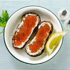 Fresh bread sandwich with red caviar and soft cheese on a plate. classic combination of ingredients. snack on the table