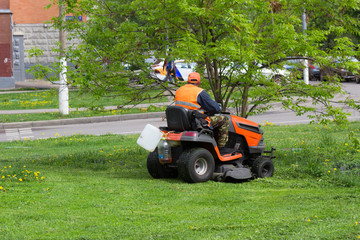 Worker municipal, city service, mows the grass on the lawn mower