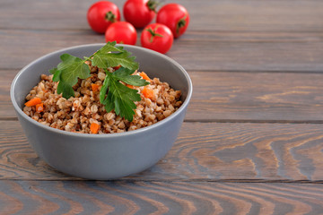 Buckwheat porridge with a sprig of parsley in a bowl and tomatoes on a dark rough wooden table. Rustic style. Traditional Russian dish.  Russian porridge