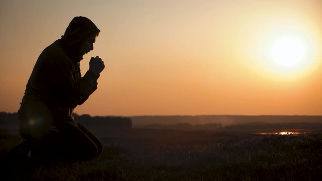 Silhouette young man praying outside at beautiful sunset. Male asks for help finding solace in faith, concept religion.
