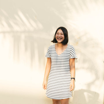 Portrait of smiling girl in striped dress with pastel yellow background with palm leaf shadows