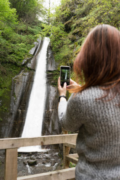 Tourist Red head woman taking pictures with mobile phone to a waterfall in the jungle
