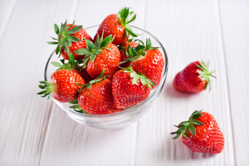 a bowl of fresh strawberries and two strawberries next to each other on a white wooden table