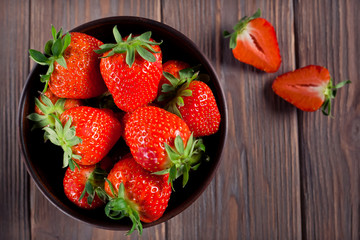 fresh ripe red strawberries in a brown bowl on a brown wooden background. top view