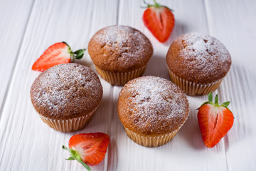 four cupcakes, muffins with strawberries on a white wooden background