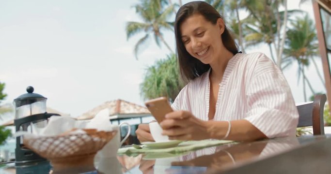 Attractive woman 30 years old sitting by the pool using a smartphone and drinking coffee. tracking shot. in slow motion. Shot on Canon 1DX mark2 4K camera