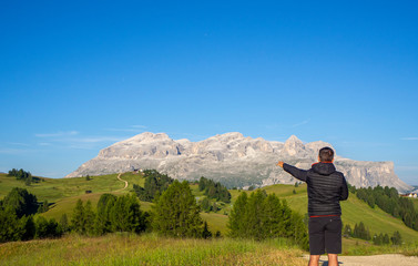 Fototapeta na wymiar A person admires the fantastic Dolomites in Italy during the summer period. The massive Sella in the background. Hiker photographed from behind. Dolomites a Unesco World Heritage