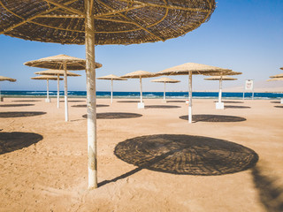Fototapeta na wymiar Toned image of empty sea beach with lots of straw umbrellas for sun protection. Crisis in tourism and travel