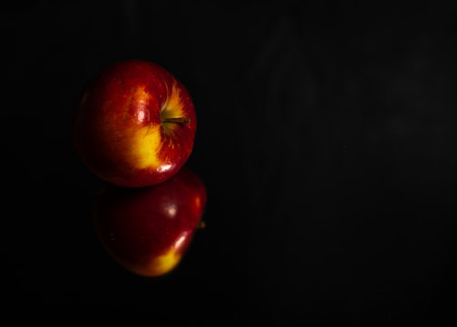 Fresh red apple reflection on black mirror surface. Close up