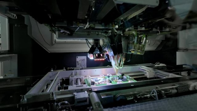Factory Machine at Work: Printed Circuit Board Being Assembled with Automated Robotic Arm, Surface Mounted Technology Connecting Microchips to the Motherboard. Time Lapse Macro Close-up Footage