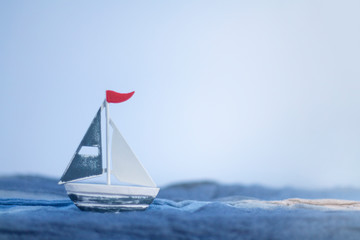 Iron toy ship with red flag on the blue fabric waves