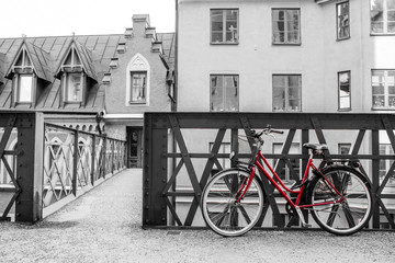 Fototapeta na wymiar A picture of a lonely red bike standing in the typical street in Stockholm by the bridge to a house. The bike looks to be modern in a retro style. The background is black and white. 