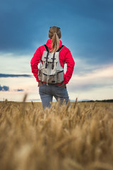 Naklejka na ściany i meble Hiking woman standing in wheat field and enjoying view to beautiful landscape with dramatic sky