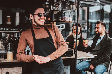 Attractive cheerful barista in sunglasses took a coffeebreak at his own coffeeshop.