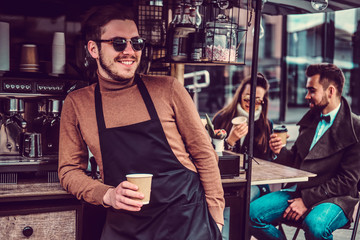 Fototapeta na wymiar Attractive cheerful barista in sunglasses took a coffeebreak at his own coffeeshop.