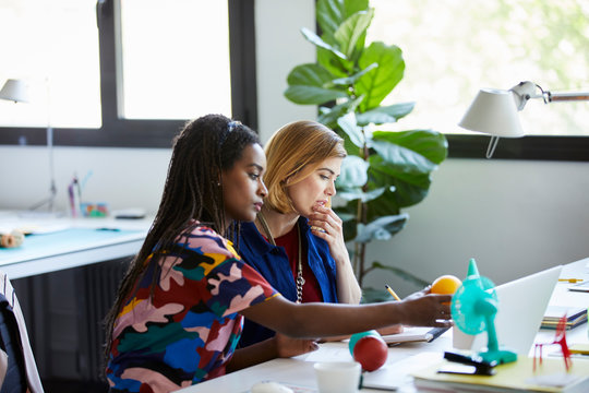 Graphic Designers Discussing Over Objects At Desk - Powered by Adobe