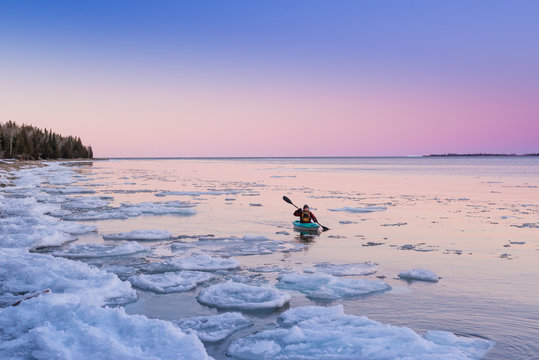 Man alone kayaking icy lake in Ontario wilderness