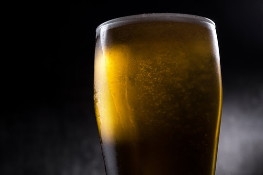 Cold beer glass with condensation and bubbles over grey concrete background