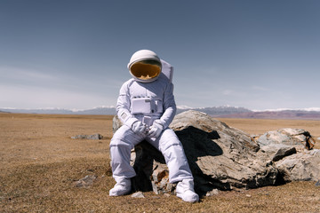 Person in space suit sitting on rock