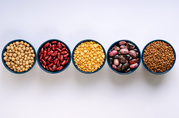 A variety of legumes. Lentils, chickpeas, peas and beans in blue bowls on a white background. Top view.