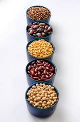 A variety of legumes. Lentils, chickpeas, peas and beans in blue bowls on a white background. Close-up