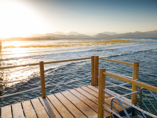 Fototapeta na wymiar Beautiful view from the wooden pier or bridge on calm ocean sea waves and sunset over the mountains