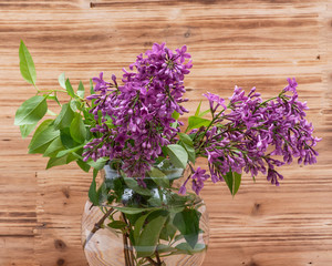 Fresh cut Purple Lilac Flowers in clear glass vase on wooden background. Syringa vulgaris.