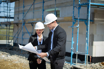 Two architects a man and a woman in construction in white helmets.