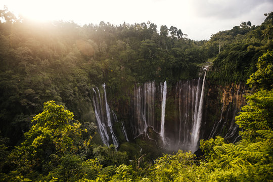 tumpak sewu waterfall in green lush jungle at sunset
