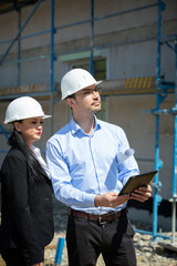Two architects a man and a woman in construction in white helmets.