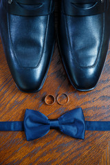 gold wedding rings lie on the table next to the men's bow tie and shoes
