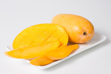 Yellow mango and slices of mango are on the white plate.  Isolated background