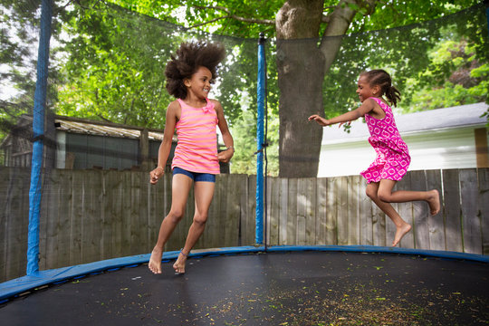 Portrait of a young girl, jumping happily in a large enclosed trampoline with her sister.
